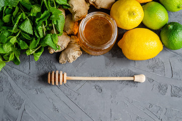 Citrus fruits lemons and lime, ginger root, mint leaves, fresh honey in a jar on a dark background.