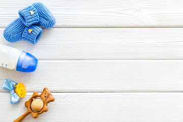 Blue knitted footwear and rattle, bottle, dummy for baby on white wooden background top view mockup