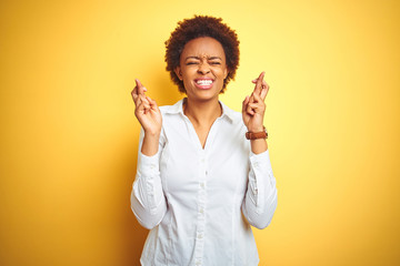 African american business woman over isolated yellow background gesturing finger crossed smiling with hope and eyes closed. Luck and superstitious concept.