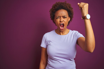 Young beautiful african american woman with afro hair over isolated purple background angry and mad raising fist frustrated and furious while shouting with anger. Rage and aggressive concept.