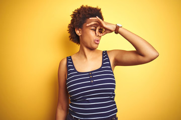 Beauitul african american woman wearing summer t-shirt over isolated yellow background smelling something stinky and disgusting, intolerable smell, holding breath with fingers on nose