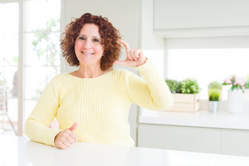 Beautiful senior woman wearing yellow sweater smiling and confident gesturing with hand doing size sign with fingers while looking and the camera. Measure concept.