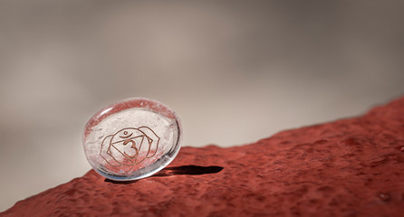 Closeup small translucent Reiki stone with chakra ornament placed on rough surface on blurred gray background