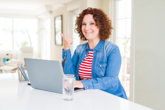 Senior woman working using computer laptop pointing and showing with thumb up to the side with happy face smiling