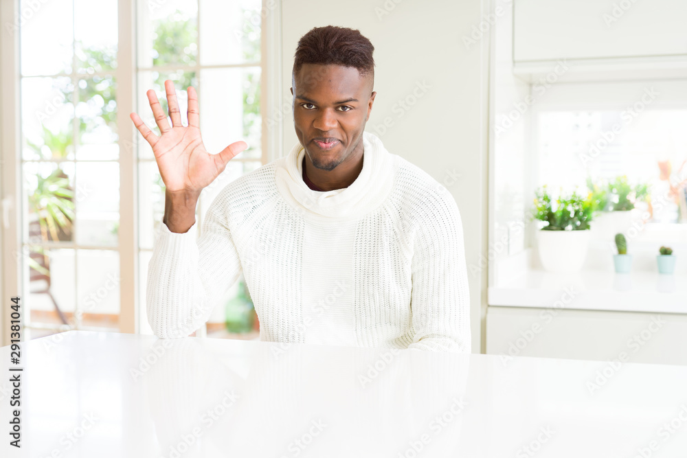 Sticker Handsome african american man on white table showing and pointing up with fingers number five while smiling confident and happy.