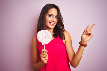 Young beautiful woman eating sweet candy over pink isolated background very happy pointing with hand and finger to the side