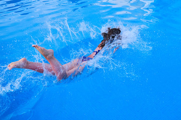 Fototapeta na wymiar The girl jumps into the pool, the moment of immersion in the water and flying spray