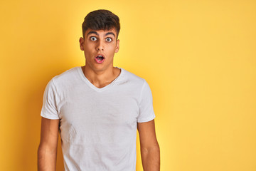 Fototapeta premium Young indian man wearing white t-shirt standing over isolated yellow background afraid and shocked with surprise and amazed expression, fear and excited face.