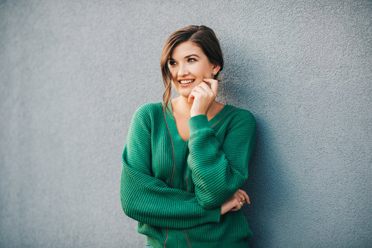 Outdoor portrait of beautiful young woman with wavy hairstyle, wearing knitted green pullover