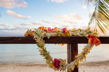 A beautiful lei of flowers rests on a the railing of a wooden deck overlooking a lagoon in French...