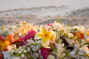 A lei of beautiful tropical flowers rests on a railing above a white sandy beach - obrazy, fototapety, plakaty