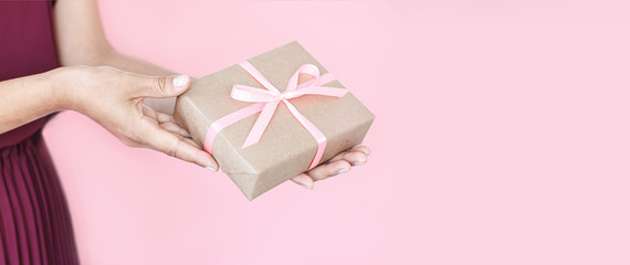 Woman hands holding present box with pinlk bow on pastel pink background