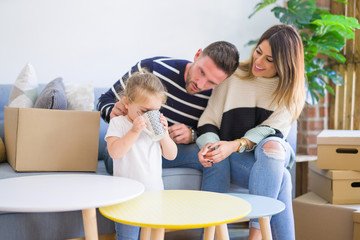 Beautiful family, parents sitting on the sofa drinking coffee looking his kid playing at new home around cardboard boxes