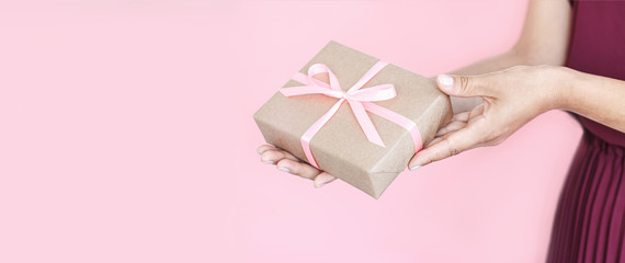 Woman hands holding present box with pinlk bow on pastel pink background