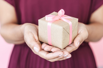 Woman hands holding present box with pinlk bow on pastel pink background