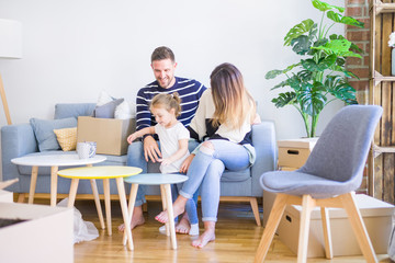 Beautiful family, parents sitting on the sofa drinking coffee looking his kid playing at new home around cardboard boxes