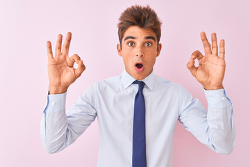 Young handsome businessman wearing shirt and tie standing over isolated pink background looking surprised and shocked doing ok approval symbol with fingers. Crazy expression