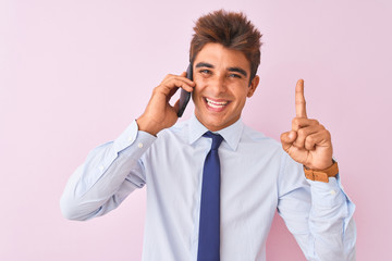 Young handsome businessman talking on the smartphone over isolated pink background surprised with an idea or question pointing finger with happy face, number one