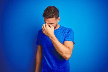 Young handsome man wearing casual t-shirt over blue isolated background tired rubbing nose and eyes...