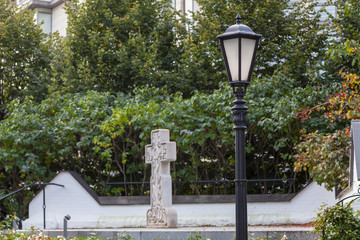 An old street lamp in the courtyard of the monastery. In the background is a stone cross