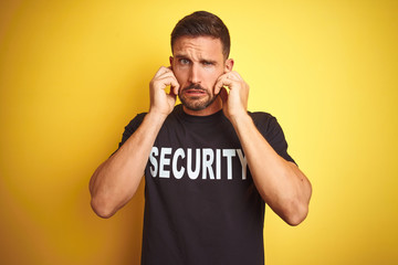 Young safeguard man wearing security uniform over yellow isolated background covering ears with...