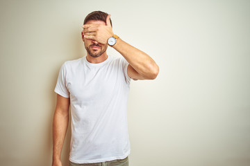 Young handsome man wearing casual white t-shirt over isolated background covering eyes with hand, looking serious and sad. Sightless, hiding and rejection concept