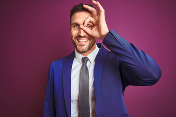 Young handsome business man over purple isolated background doing ok gesture with hand smiling, eye looking through fingers with happy face.