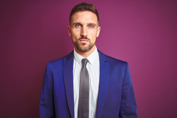 Young handsome business man over purple isolated background with serious expression on face. Simple and natural looking at the camera.