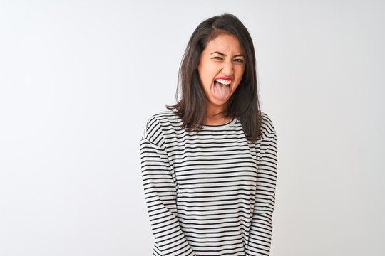 Young beautiful chinese woman wearing striped t-shirt standing over isolated white background sticking tongue out happy with funny expression. Emotion concept.