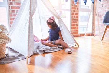 Beautiful toddler girl sitting on the floor playing with unicorn and doll inside  tipi at...