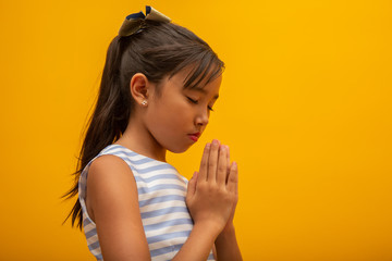 Little girl praying on yellow background. Little asian girl hand praying, hands folded in prayer...