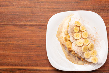 Tapioca filled with banana, cinnamon and condensed milk, on wooden background. Flatbread made from...