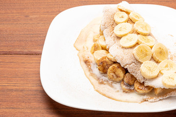 Tapioca filled with banana, cinnamon and condensed milk, on wooden background. Flatbread made from cassava (also known as casabe, bammy, beiju, bob, biju).