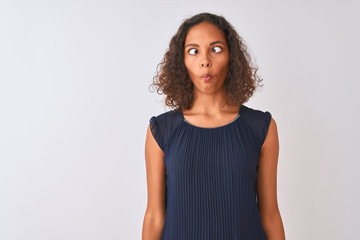 Young brazilian woman wearing blue dress standing over isolated white background making fish face with lips, crazy and comical gesture. Funny expression.