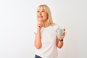Middle age woman drinking cup of coffee standing over isolated white background serious face...