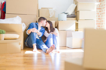 Young beautiful couple relaxing sitting on the floor around cardboard boxes at home, smiling happy moving to a new house