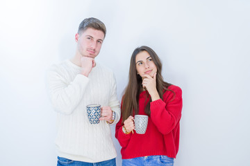Beautiful young couple over white isolated background drinking a cup of coffee serious face...