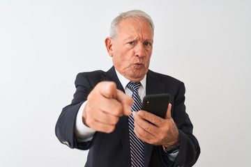 Senior grey-haired businessman using smartphone standing over isolated white background pointing with finger to the camera and to you, hand sign, positive and confident gesture from the front