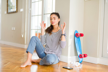 Young woman sitting on the floor using skateboard and headphones relax and smiling with eyes closed...