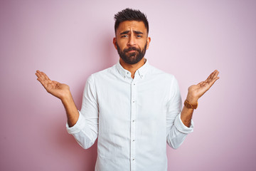 Young indian businessman wearing elegant shirt standing over isolated pink background clueless and...