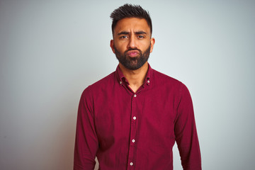 Young indian man wearing red elegant shirt standing over isolated grey background looking at the camera blowing a kiss on air being lovely and sexy. Love expression.