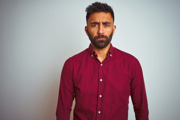 Young indian man wearing red elegant shirt standing over isolated grey background depressed and worry for distress, crying angry and afraid. Sad expression.