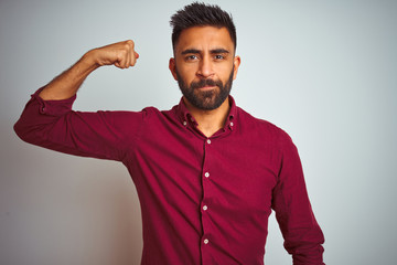 Obraz premium Young indian man wearing red elegant shirt standing over isolated grey background Strong person showing arm muscle, confident and proud of power