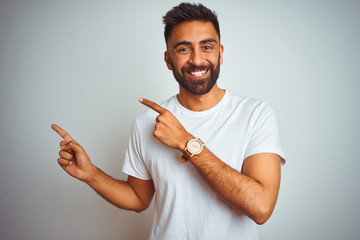 Young indian man wearing t-shirt standing over isolated white background smiling and looking at the...
