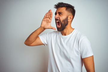 Young indian man wearing t-shirt standing over isolated white background shouting and screaming loud to side with hand on mouth. Communication concept.