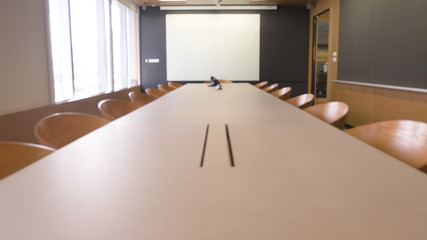 empty wood table with blur meeting room with white screen.
