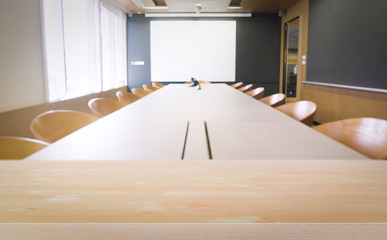 empty wood table with blur meeting room with white screen.