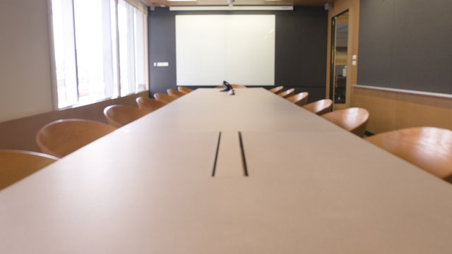 Empty Wood Table With Blur Meeting Room With White Screen.