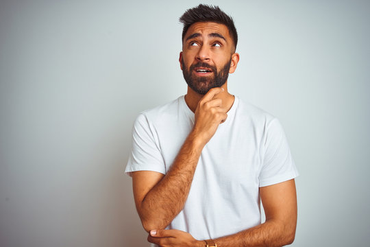 Young indian man wearing t-shirt standing over isolated white background Thinking worried about a question, concerned and nervous with hand on chin