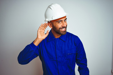 Handsome indian worker man wearing uniform and helmet over isolated white background smiling with...